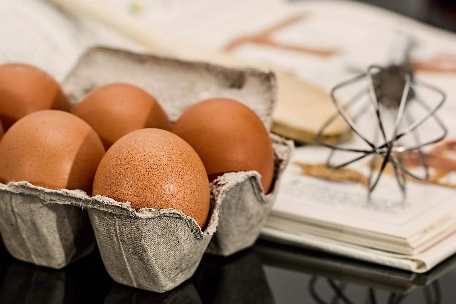 Eggs and whisk on the table with a cookbook