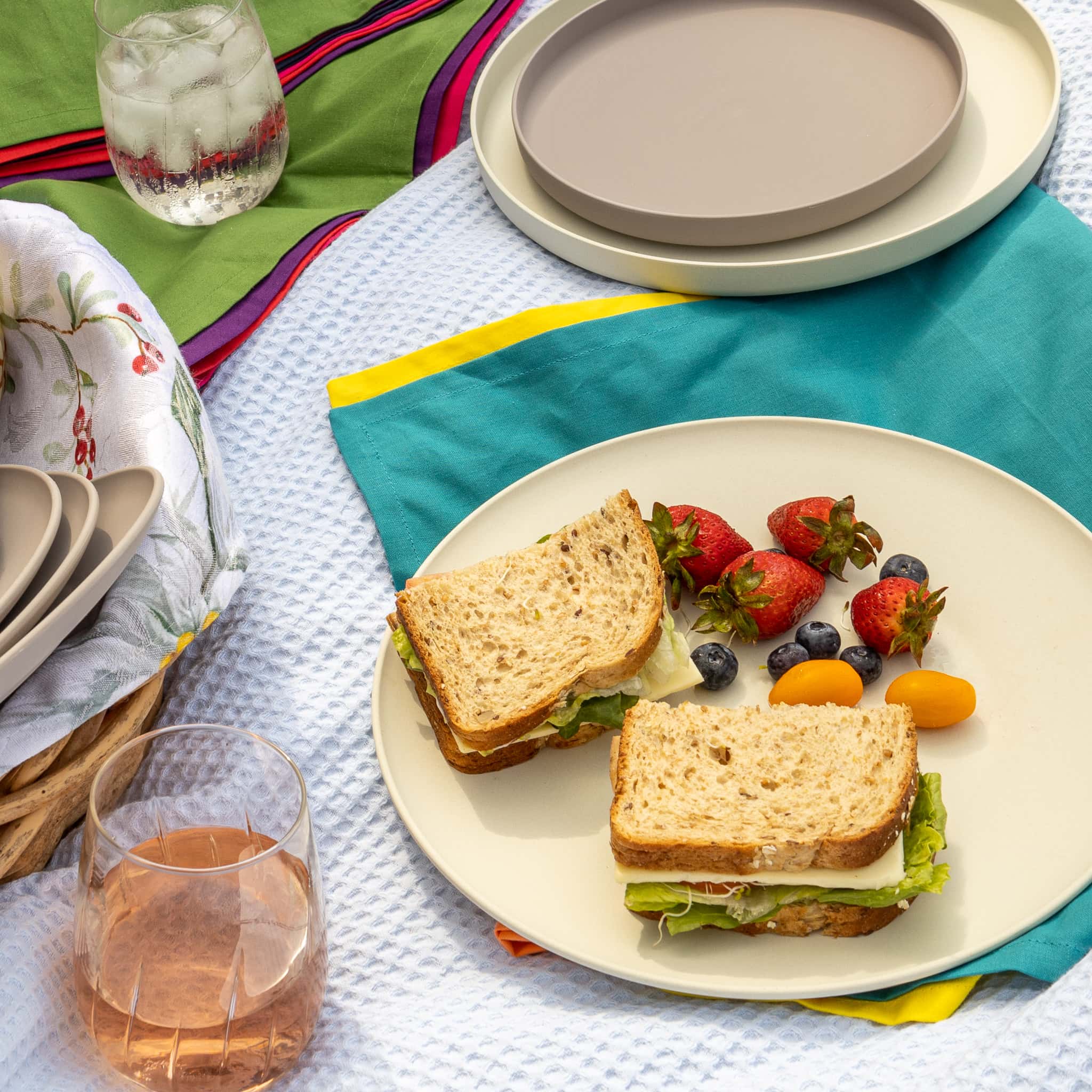 Summer picnic spread with sandwiches and strawberries on off-white non-toxic plate.